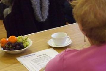 Person sitting at table with a coffee and Healthwatch literature